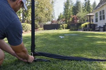 A golfer secures the frame of a backyard practice net before setting up a home hitting station.