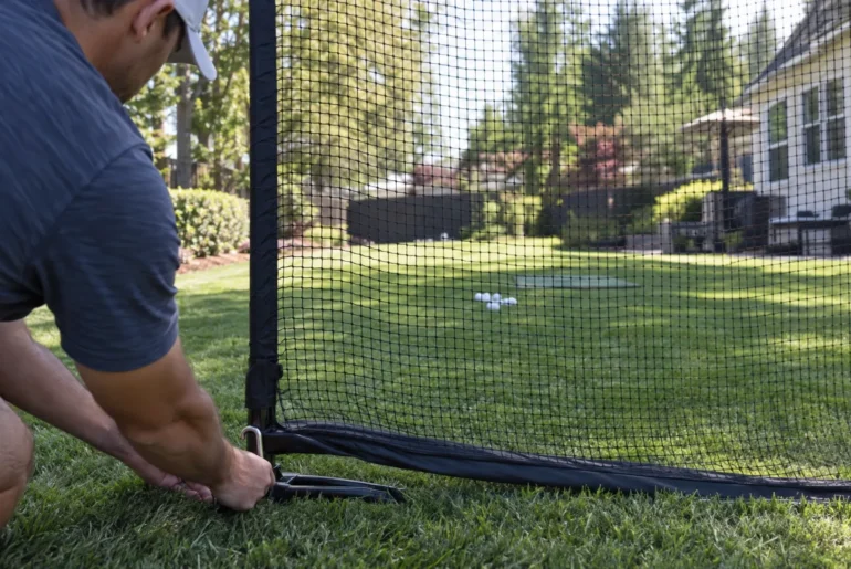 A golfer secures the frame of a backyard practice net before setting up a home hitting station.